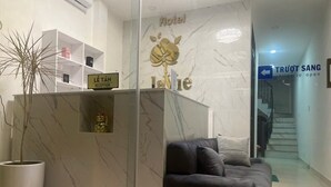 Ένας χώρος υποδοχής ξενοδοχείου με έναν μάρμαρινο πάγκο υποδοχής, έναν καναπέ, ένα φυτό σε γλάστρα και μια σκάλα στο βάθος.