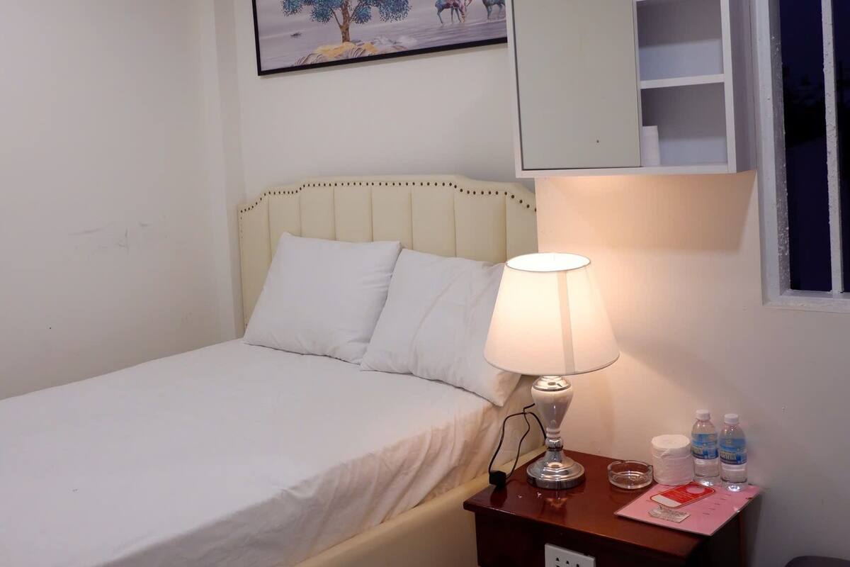 A bedroom with a bed, bedside table, lamp, and a wall-mounted shelf.
