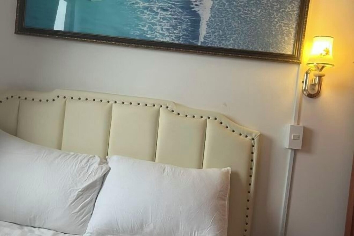 A bed with a headboard, a wall-mounted light, and a framed picture above the bed.