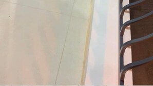 Ένας διάδρομος με μια γυάλινη πόρτα που οδηγεί σε ένα δωμάτιο, ένα μεταλλικό προστατευτικό κιγκλίδωμα και ένα δάπεδο με πλακάκια.