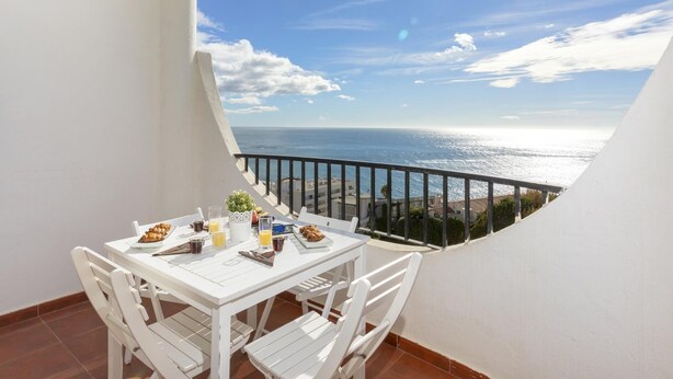 A balcony with a white table set for breakfast, overlooking a coastal view with the sea and buildings in the distance. - Sunstay Diamond Loft Fuengirola Beach (Fuengirola)