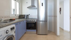 A compact kitchen with a built-in oven, a stainless steel refrigerator, a washing machine, and a window providing natural light. - Sunstay Diamond Loft Fuengirola Beach (Fuengirola)