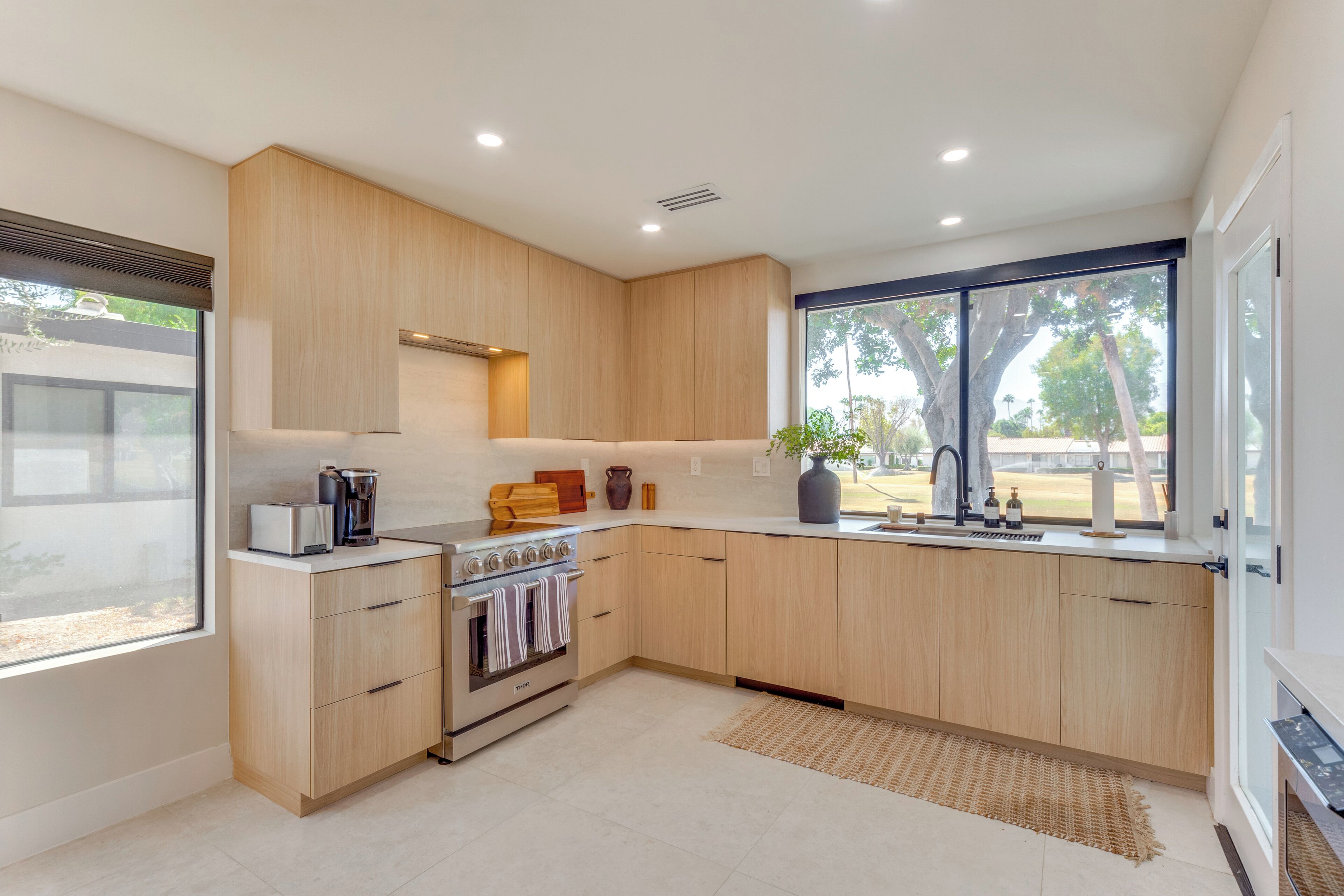 A modern kitchen with wooden cabinets, a built-in oven, and a large window providing a view of the outdoors.