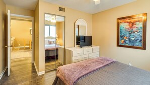 Un dormitorio con cama, cómoda, televisor, un cuadro y ventilador de techo.