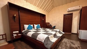 Un dormitorio con una cama de madera, una mesita de noche, un escritorio y una silla. Se ve una puerta y un equipo de aire acondicionado en la pared.