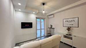 A modern living room with a sofa, a flat-screen TV, a framed sign, and a radiator. - Aster apartment - Free Parking in the historic center of Alba - Langhe (Alba)