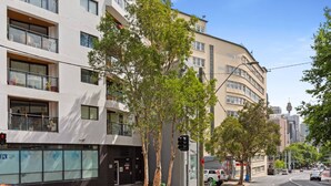 A multi-story building with balconies, a street view, and a clear sky.