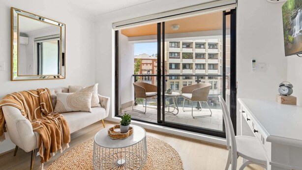 A modern living room with a sofa, a coffee table, and a view of a cityscape through large windows.
