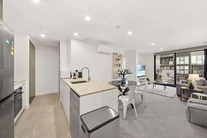 A modern kitchen with a central island, a dining area with a round table, and a living space with a sofa and a TV.