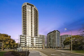A modern high-rise building with multiple balconies, surrounded by a well-maintained urban environment.