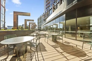 An outdoor terrace with tables and chairs, a modern building with large windows, and a clear sky.