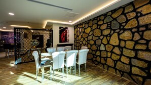 A dining area with a stone wall, a wooden floor, and a table with chairs. - Zaman Homeland Hotel (Taif)