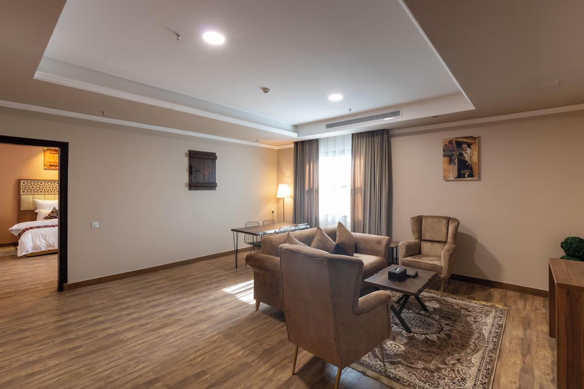 A modern hotel room with a wooden floor, a sofa, a chair, a small table, a lamp, and a painting on the wall.