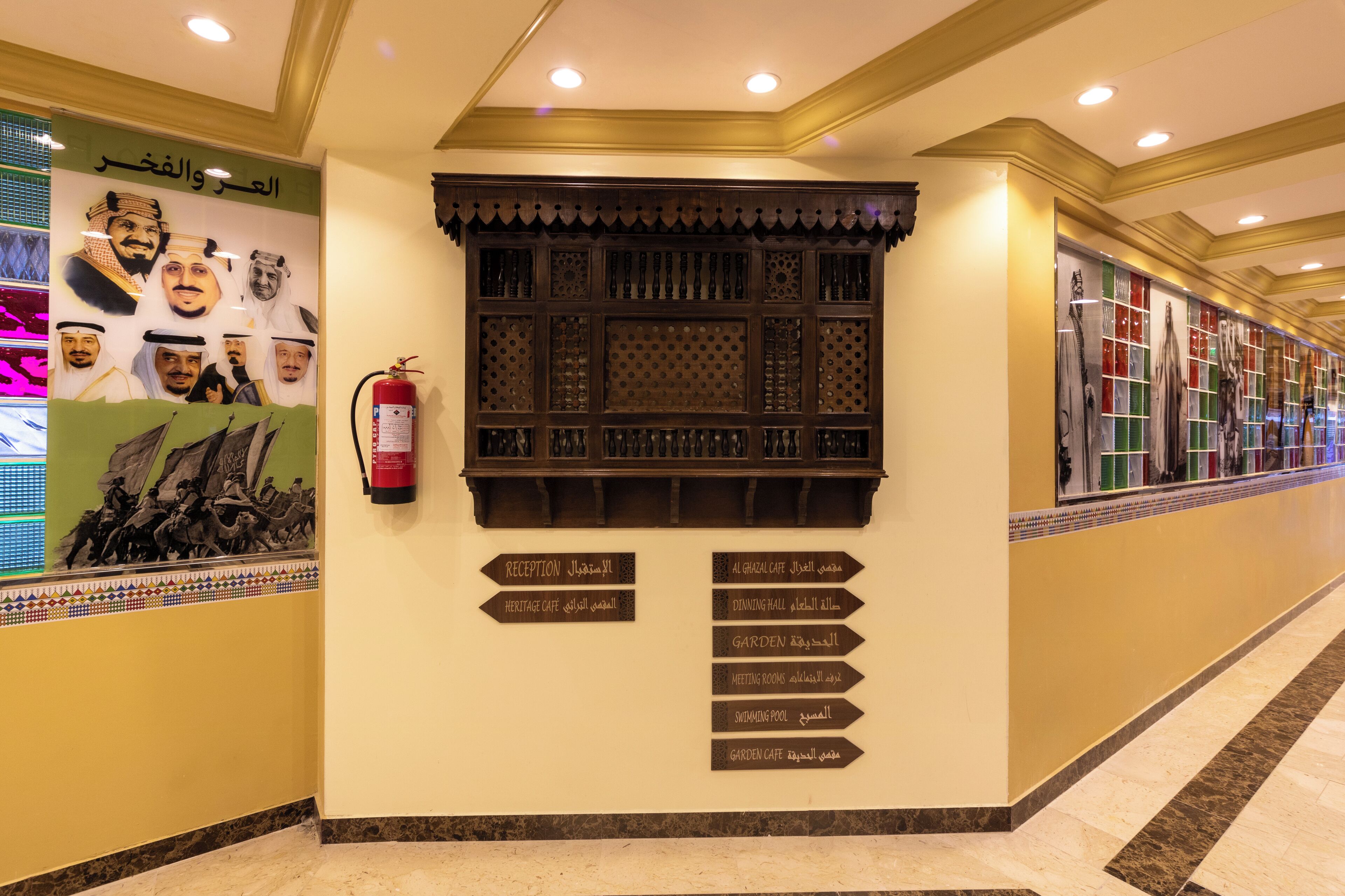 Een hotelgang met richtingwijzers, een brandblusser en een decoratieve wand met kunstwerken.