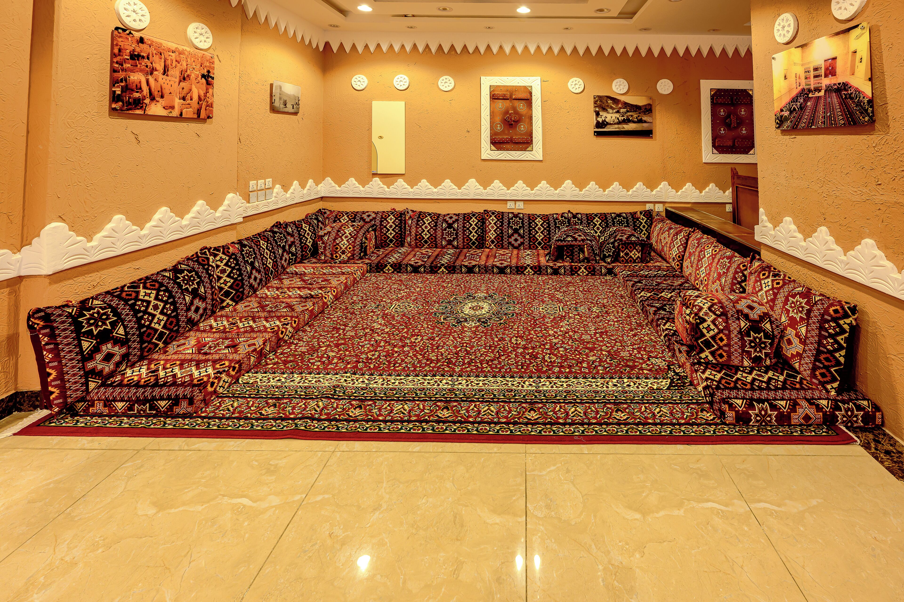 A room with a large, patterned carpet, a sofa set, and a decorative wall with clocks and framed pictures.
