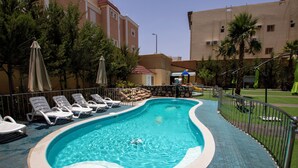 A swimming pool with lounge chairs and umbrellas, surrounded by a stone wall and greenery. - Zaman Homeland Hotel (Taif)