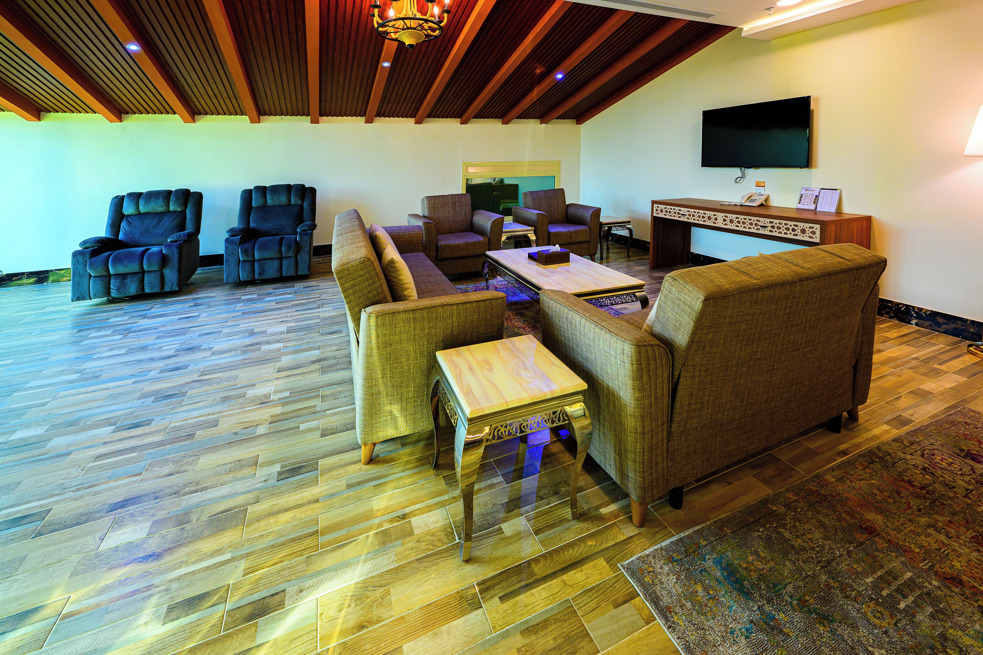 A spacious living area with a wooden ceiling, a flat-screen TV mounted on the wall, and a reception desk with a telephone and a small table.