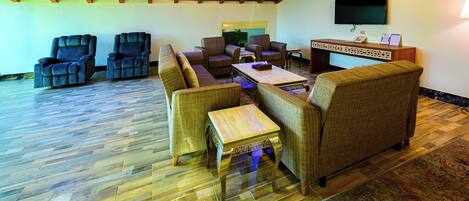 A spacious living area with a wooden ceiling, a flat-screen TV mounted on the wall, and a reception desk with a telephone and a small table.