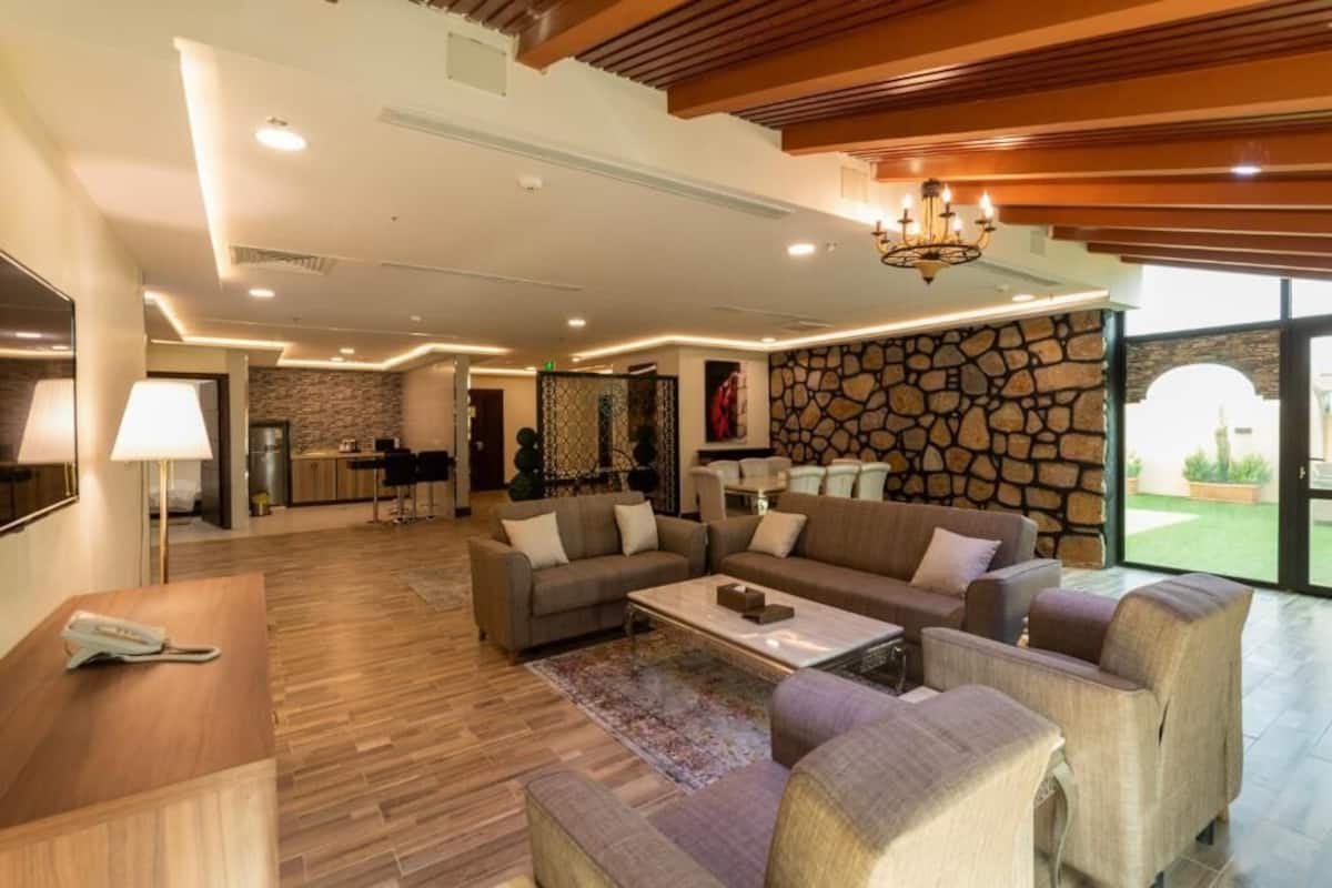 A spacious living area with a stone accent wall, a chandelier, and a modern kitchen in the background.