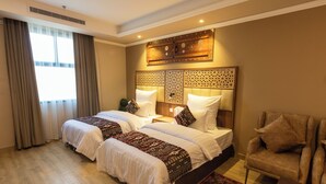 A hotel room with two beds, a sitting area, and a decorative headboard. - Zaman Homeland Hotel (Taif)