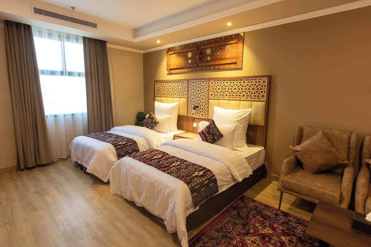 A hotel room with two beds, a sitting area, and a decorative headboard.