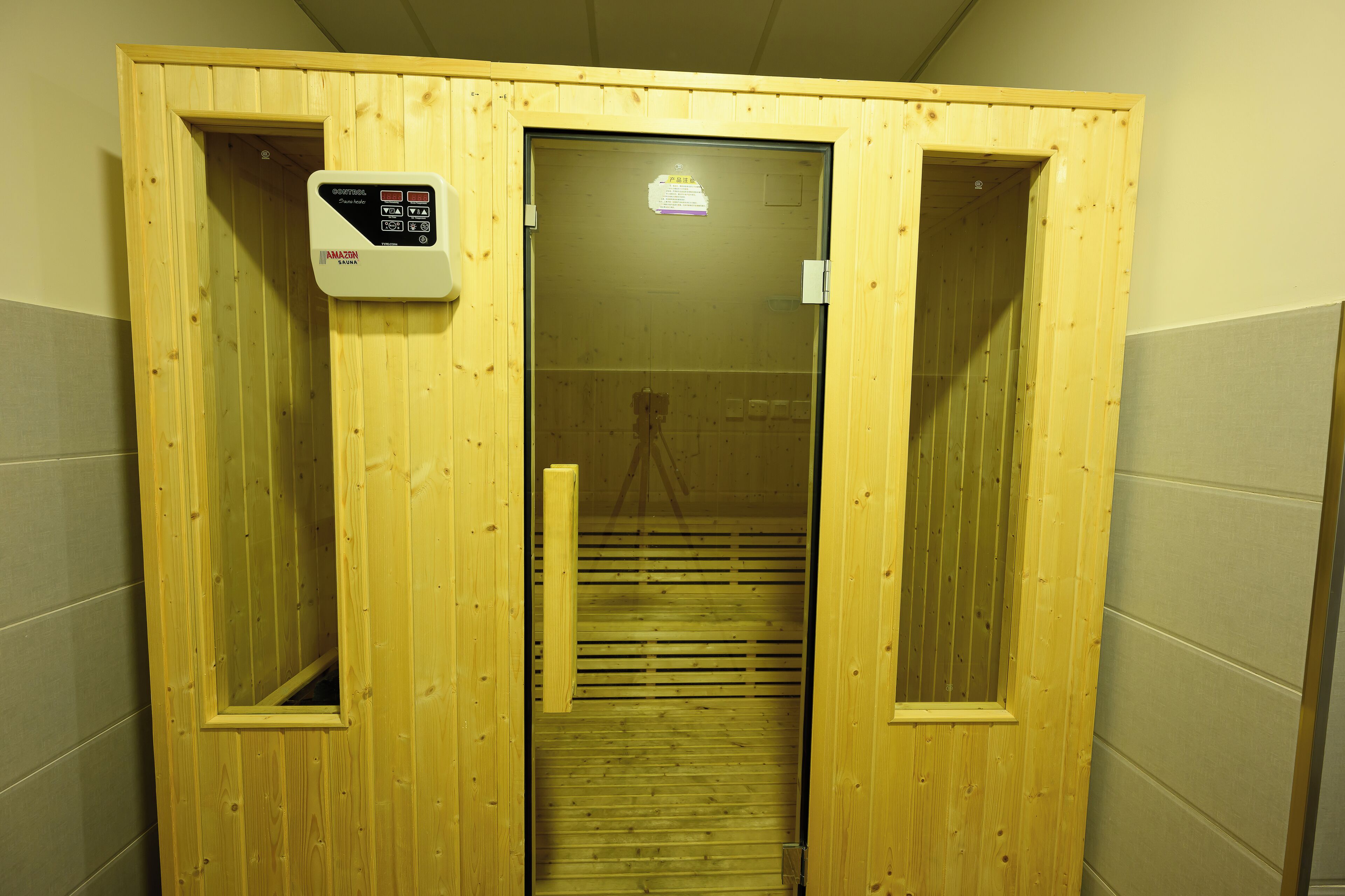 Una sauna de madera con panel de control, puerta corredera y suelo de baldosas.