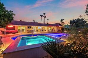 A pool area with a house in the background, surrounded by palm trees and outdoor seating. - The Rusty Cactus | Heated Salt Pool, Spa, & More! (Phoenix)