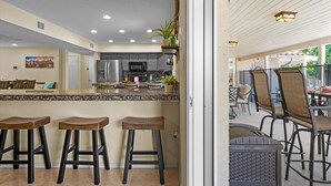 A modern kitchen with granite countertops, dark stools, and a dining area with metal chairs and a table. - The Rusty Cactus | Heated Salt Pool, Spa, & More! (Phoenix)
