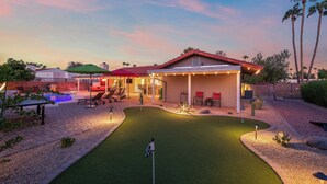 A house with a backyard featuring a putting green, patio furniture, and a covered seating area. - The Rusty Cactus | Heated Salt Pool, Spa, & More! (Phoenix)