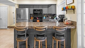 A modern kitchen with a granite countertop, stainless steel appliances, and bar stools. - The Rusty Cactus | Heated Salt Pool, Spa, & More! (Phoenix)