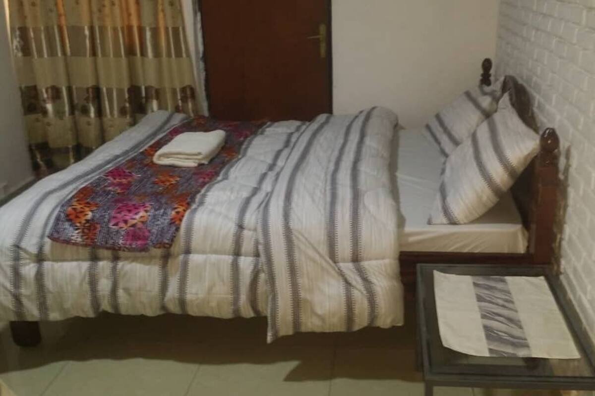 Une petite chambre à coucher, bien rangée, avec un lit simple, une table de chevet et une fenêtre avec des rideaux.