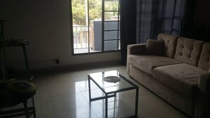 A living room with a sofa, a glass coffee table, and a view through a large window. - GreenPage Apartments Kiyovu  (Kigali)