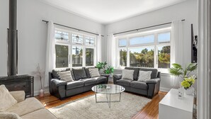 Una sala de estar moderna con chimenea, sofás de cuero, una mesa de centro de vidrio y ventanas amplias que ofrecen vista a árboles.