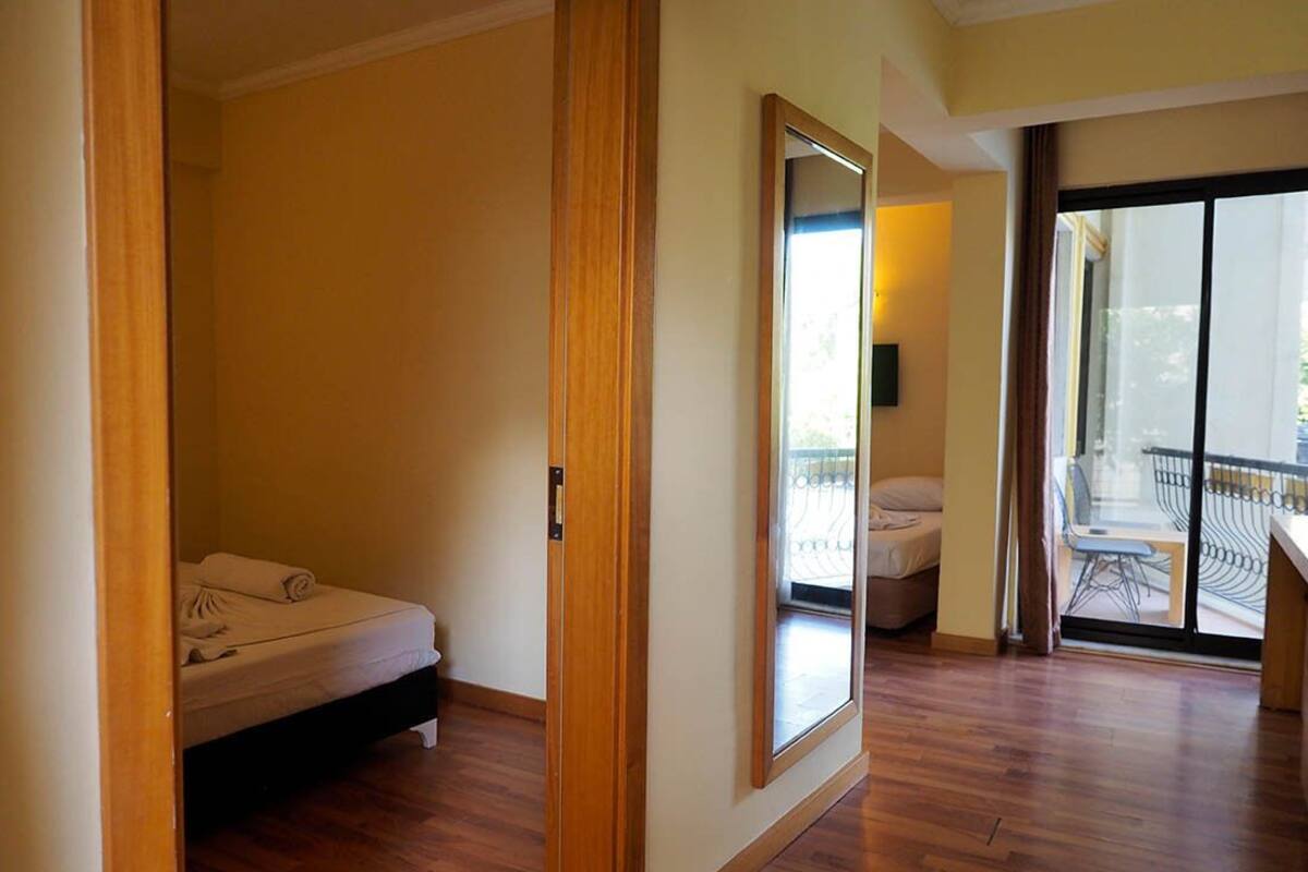 A hotel room with a wooden floor, a bed, a large mirror, and a balcony with a view.