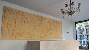 Un intérieur moderne agrémenté d’une grande sculpture en relief en bois au mur, d’un comptoir d’accueil en marbre et d’un lustre.