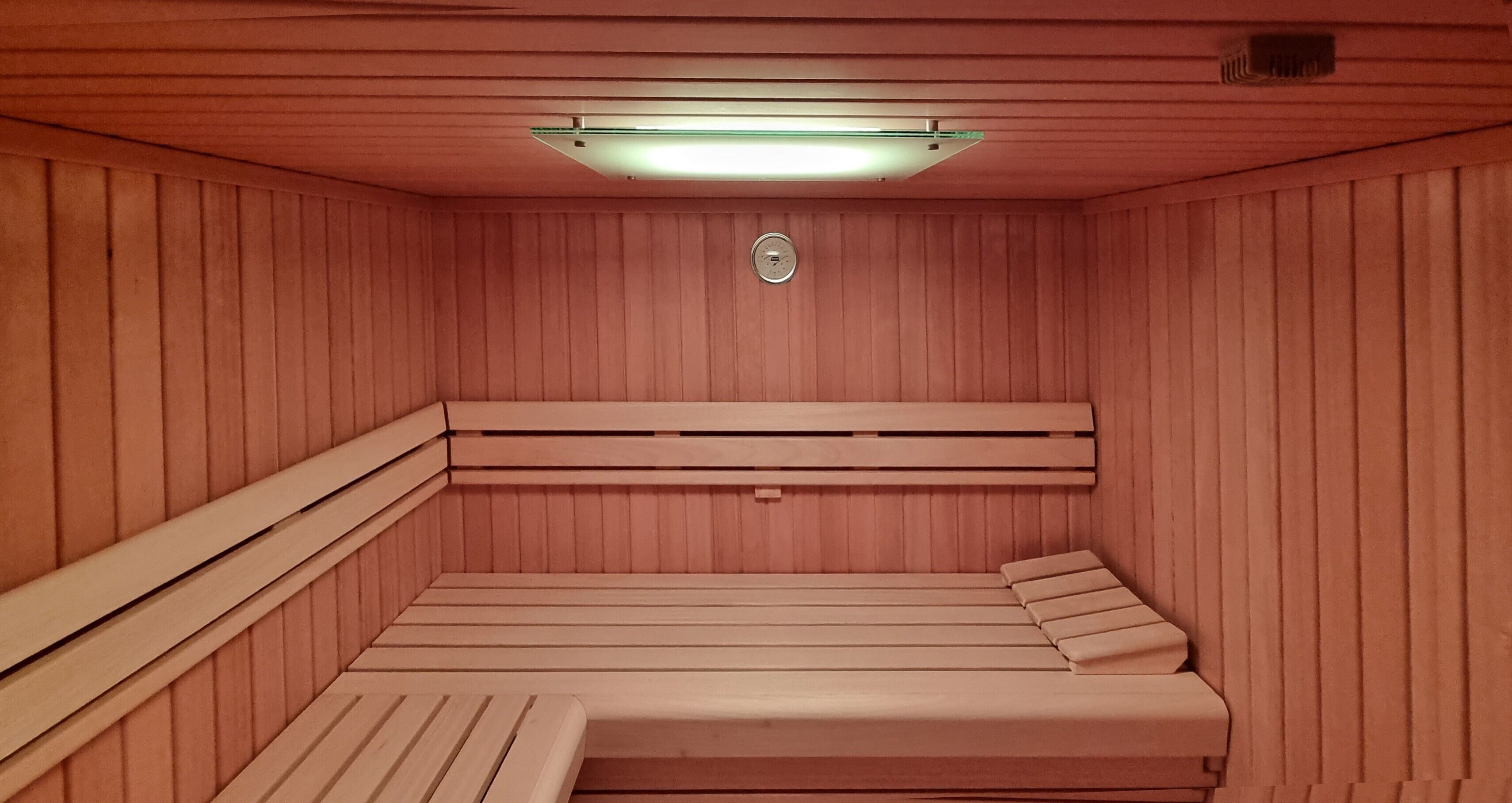 Uma sauna com paredes e bancos de madeira, uma luz no teto e um sistema de ventilação.