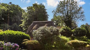 A traditional thatched-roof house surrounded by well-maintained hedges and flowering plants. - Apartment 'My Little Rose Cottage' with Private Terrace, Private Garden and Wi-Fi (Dörpling)