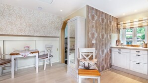 A modern kitchen with white cabinetry, a wooden dining table, and a chair with a decorative cushion. - Apartment 'My Little Rose Cottage' with Private Terrace, Private Garden and Wi-Fi (Dörpling)