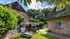 A thatched-roof house with a stone wall, a small garden with a bench and table, and a pathway leading to another building. - Apartment 'My Little Rose Cottage' with Private Terrace, Private Garden and Wi-Fi (Dörpling)