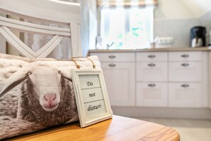 A bed with a pillow featuring a sheep's face, a bedside table, a framed sign with the text 'Do not disturb,' and a kitchen area in the background.