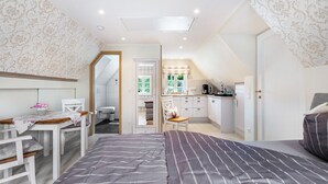 A bedroom with a bed, a desk, and a chair. There is a kitchenette in the background. - Apartment 'My Little Rose Cottage' with Private Terrace, Private Garden and Wi-Fi (Dörpling)