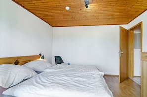 Une chambre avec un plafond en bois, un lit avec une literie blanche, une table de chevet et une porte donnant sur une salle de bain.