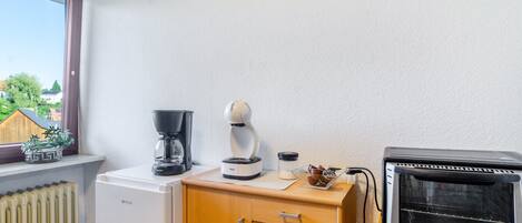 A kitchenette with a coffee maker, a toaster, a small refrigerator, and a window with a view of houses and trees.