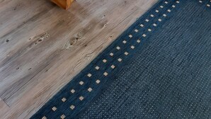 Un escalier en bois avec une rampe, un tapis bleu et trois tableaux accrochés au mur représentant des scènes de plage.