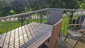 Un balcon avec une table en bois et des chaises en osier, donnant sur un paysage verdoyant.