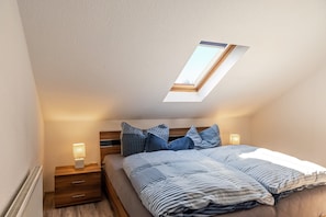 Une chambre avec un puits de lumière, un lit avec une literie à rayures, deux lampes de chevet et une table de chevet en bois.