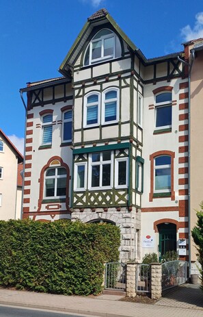 Un edificio de varios pisos con un estilo arquitectónico tradicional, que presenta una entrada destacada en esquina, numerosas ventanas y fachada de piedra.