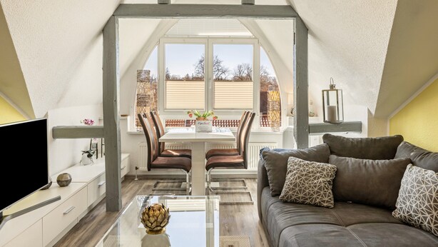 Ein modernes Schlafzimmer im Loft-Stil mit einem großen Dachfenster, einem Essbereich mit Tisch und Stühlen sowie einer gemütlichen Sitzecke mit einer Couch.