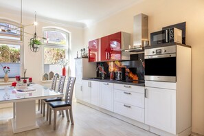 Une cuisine moderne avec des armoires blanches, des appareils en acier inoxydable et un coin repas comprenant une table et des chaises en verre.