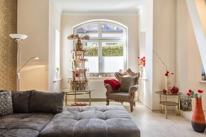Un salon comprenant un canapé, un fauteuil, une colonne décorative et un vase avec des fleurs.